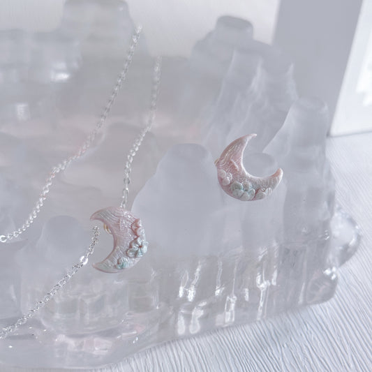 Pair of moon-shaped earrings with floral details on a clear stand.