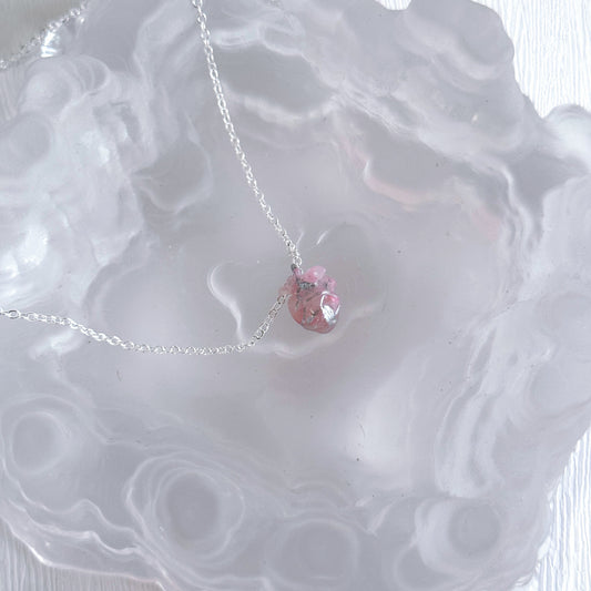 Necklace with a pink heart pendant on a textured white surface