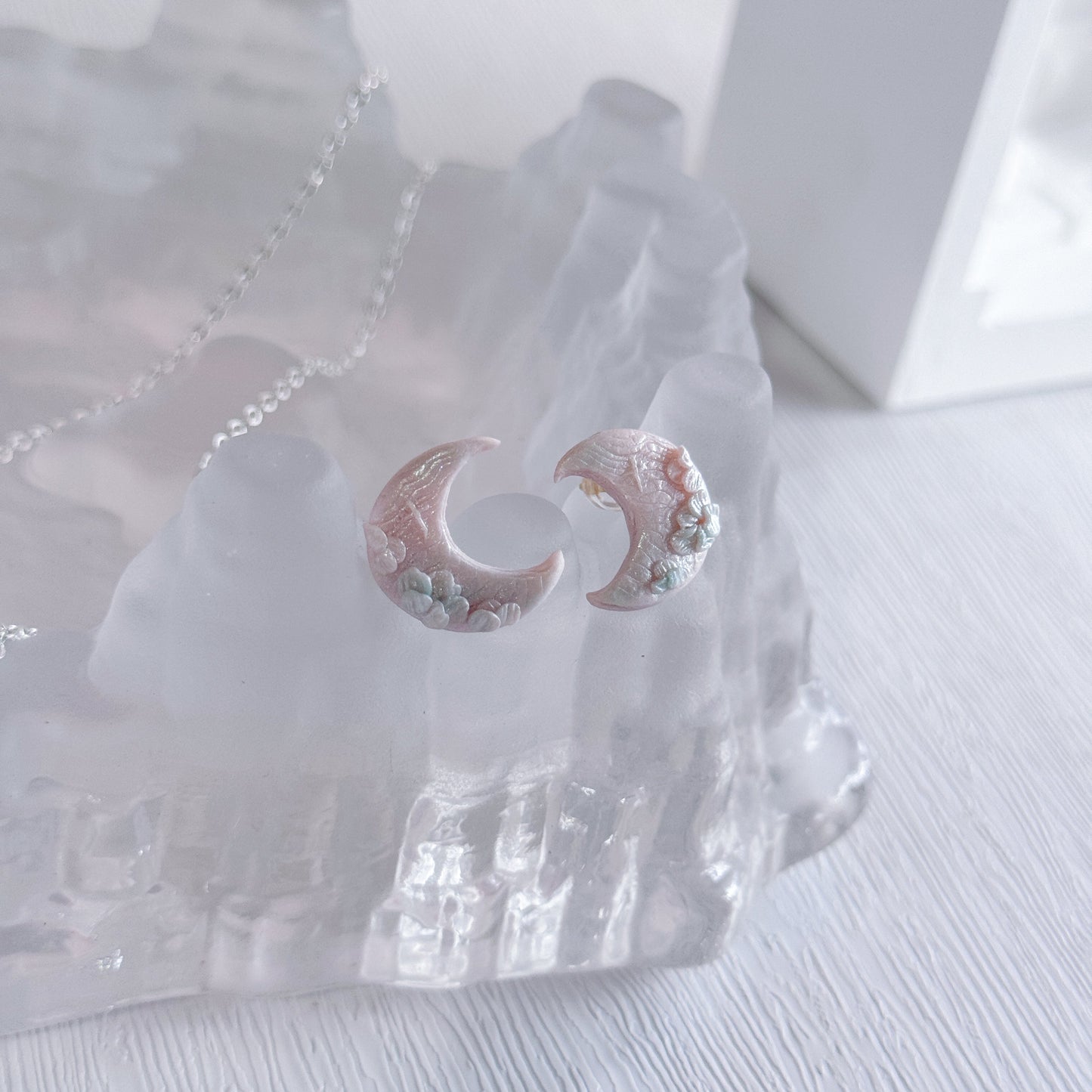 Pair of earrings with a moon design on a clear stand against a white background