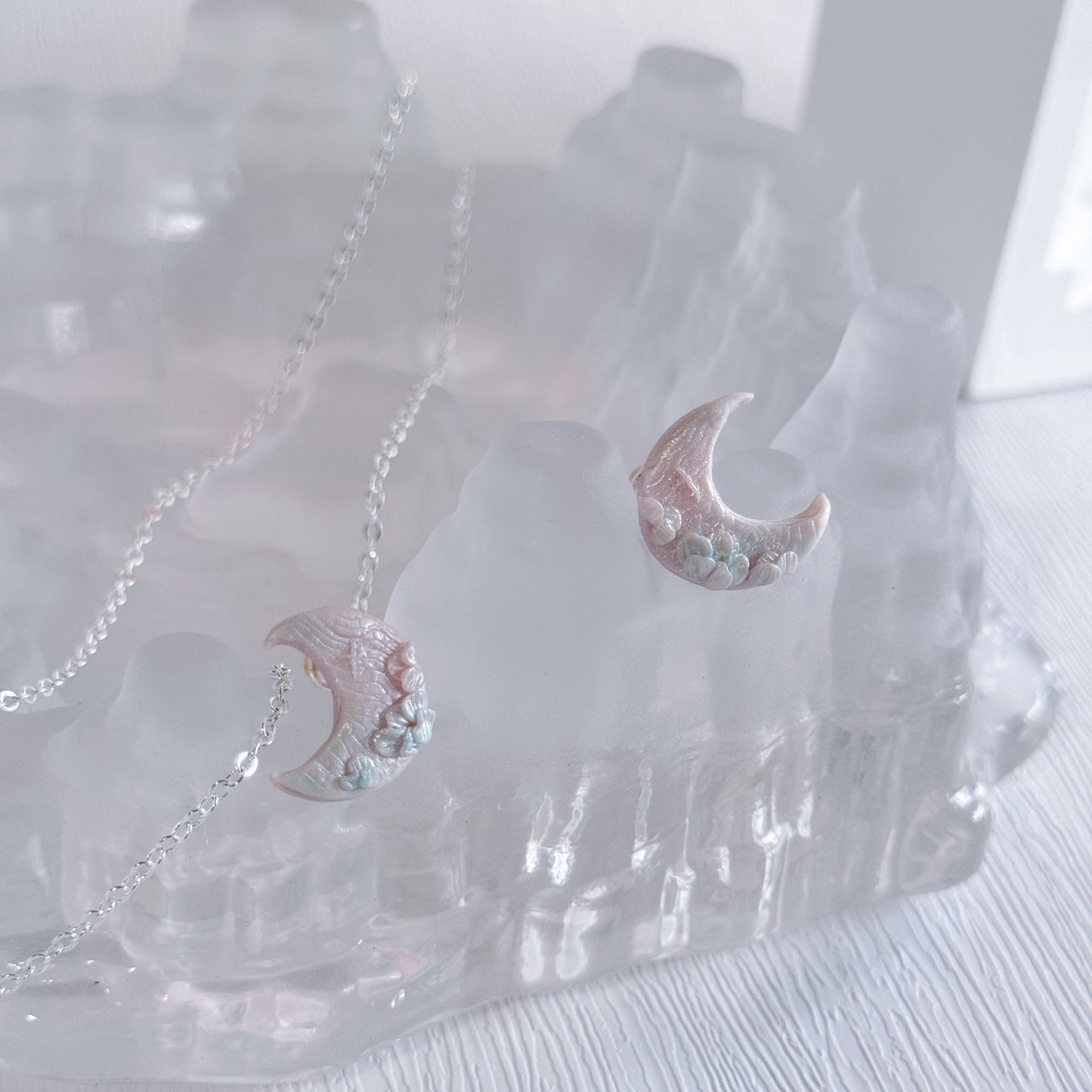 Pair of moon-shaped earrings with floral details on a clear stand.