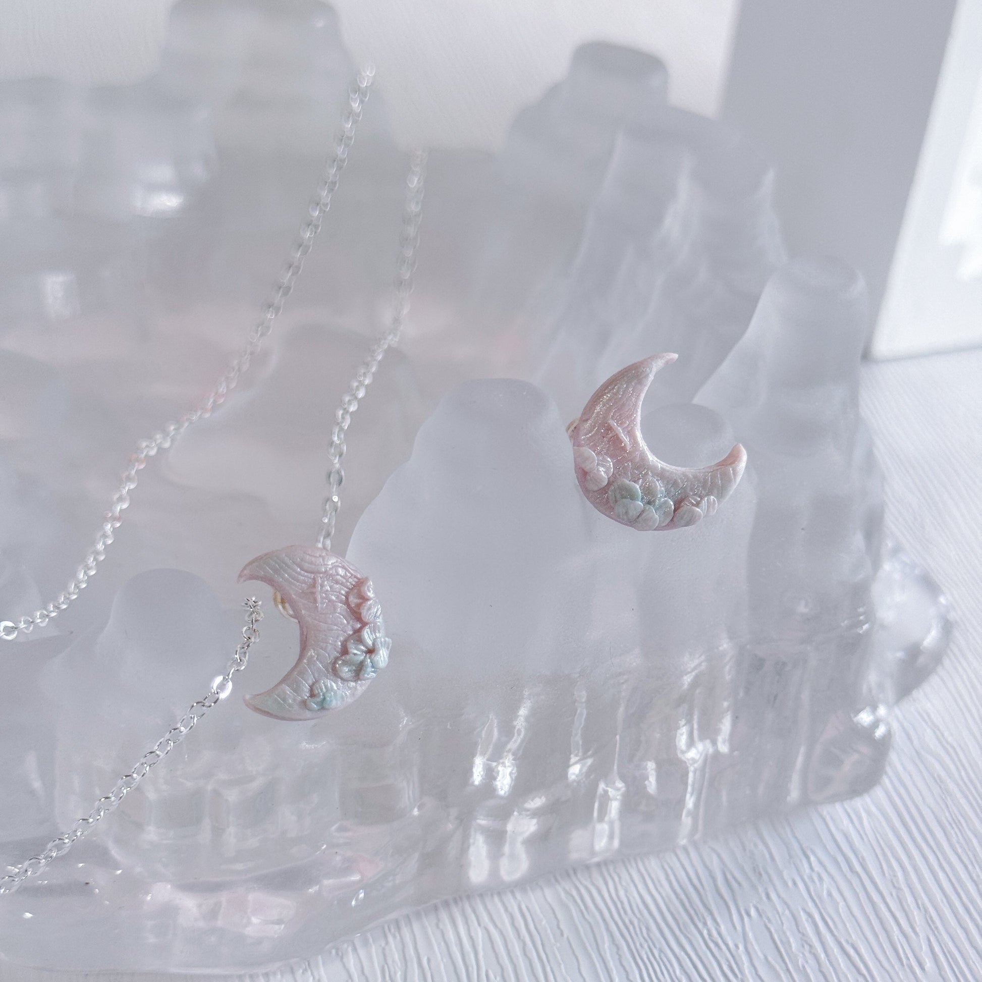 Pair of moon-shaped earrings with floral details on a clear stand.