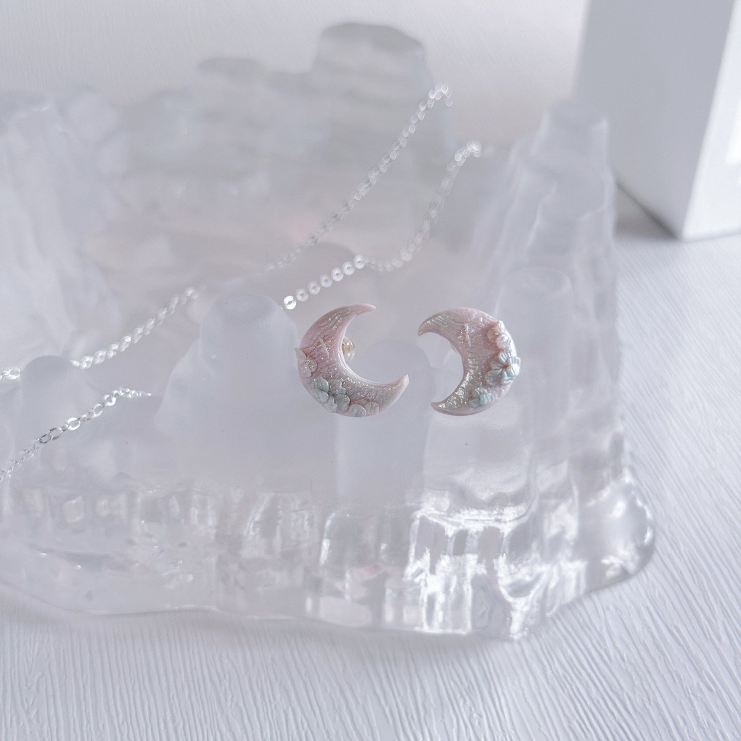 Shimmery moon-shaped earrings in clear packaging on a white surface