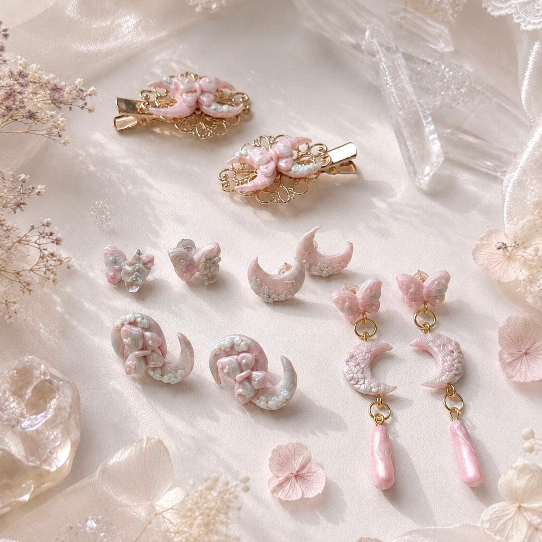 Set of decorative hair clips and earrings on a soft, textured surface with butterflies and moon.