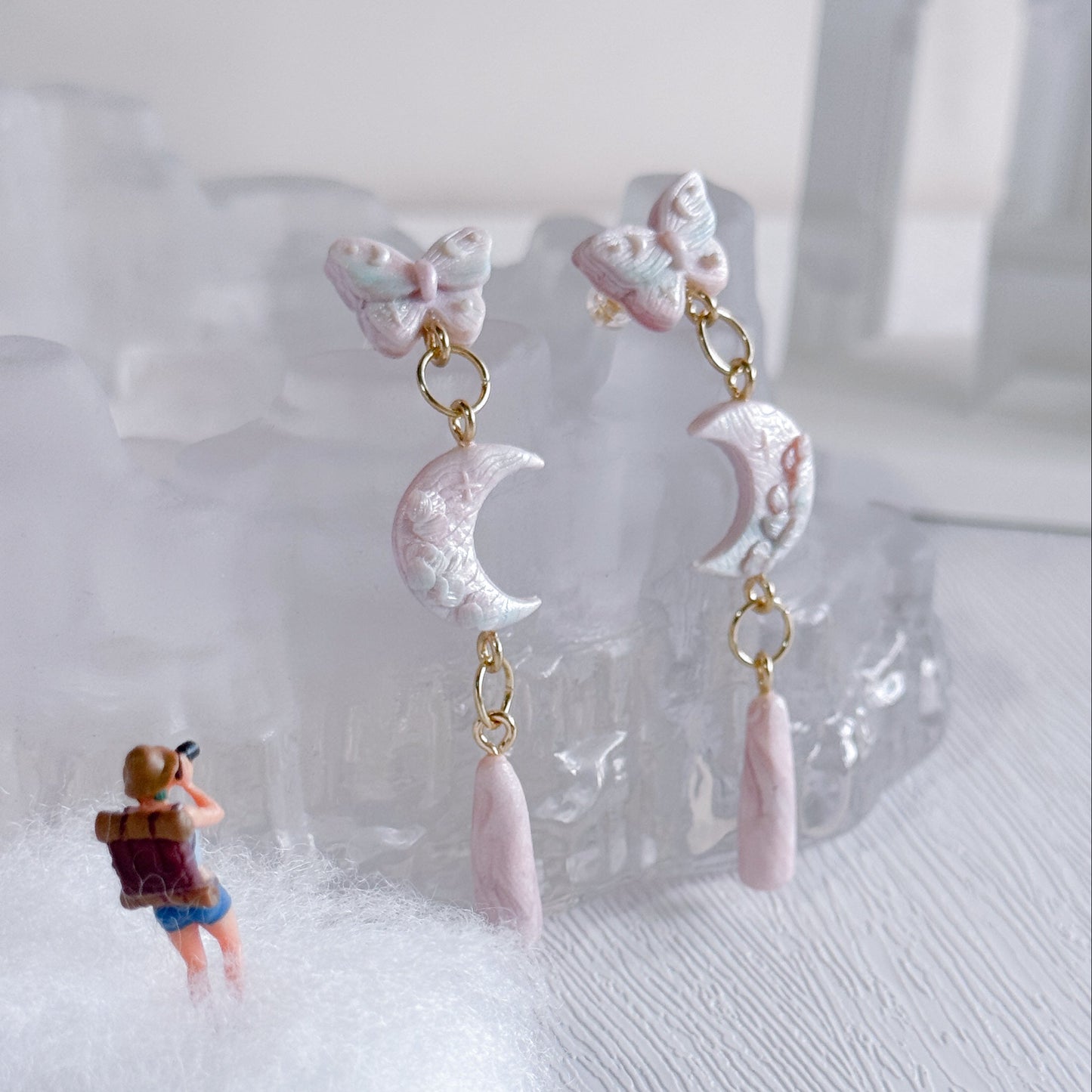 Pair of earrings with moon and pink teardrop design on a white surface.
