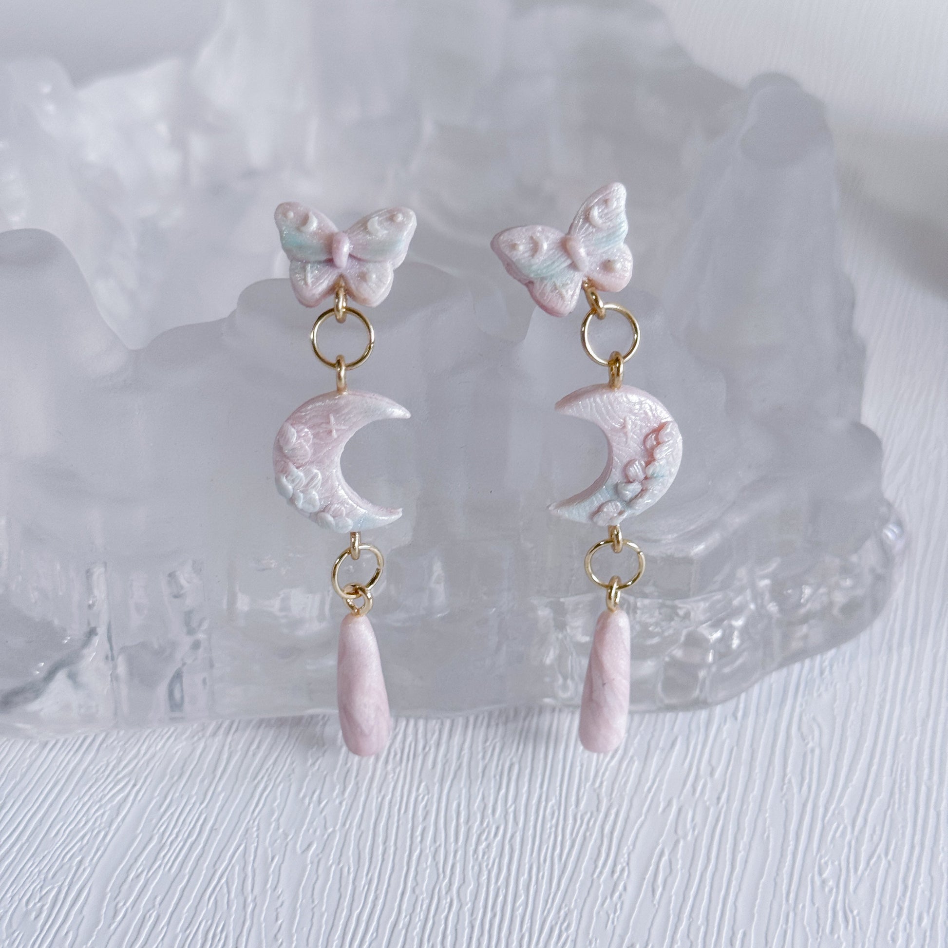 Pair of earrings with butterfly and moon design on a white background