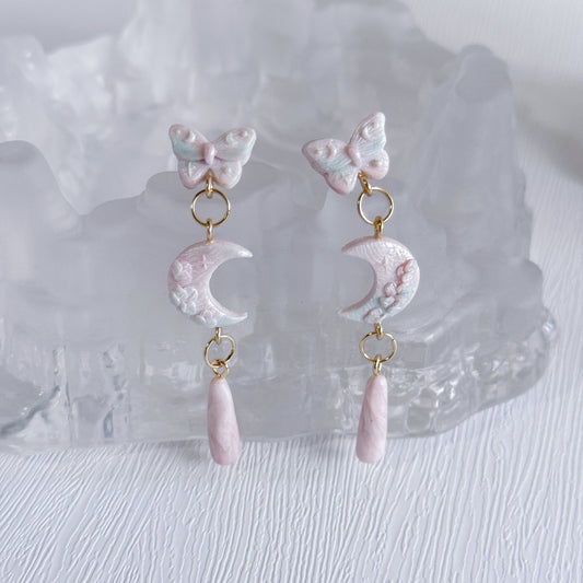 Pair of earrings with butterfly and moon design on a white background