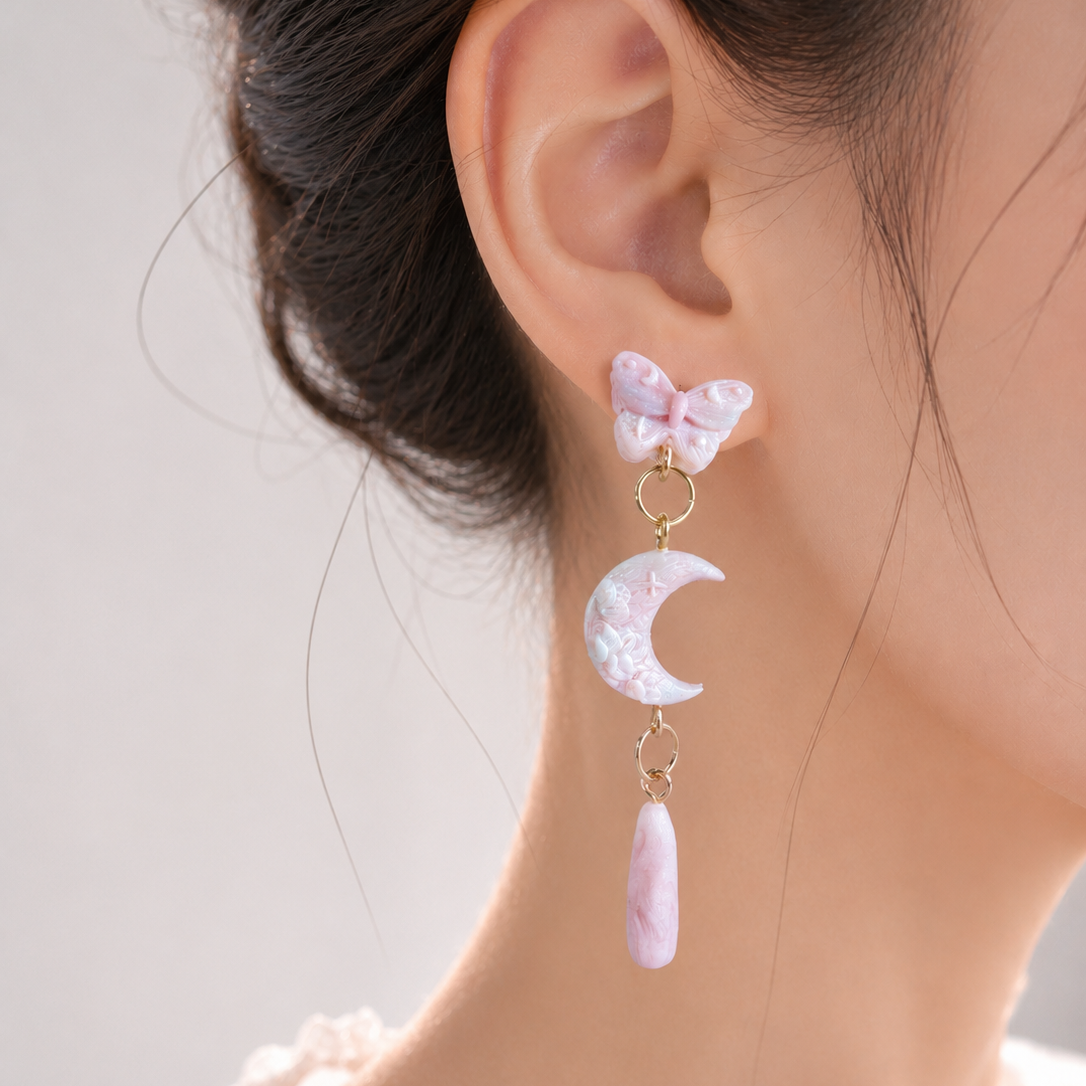 Earring with butterfly and moon design worn by a person against a neutral background