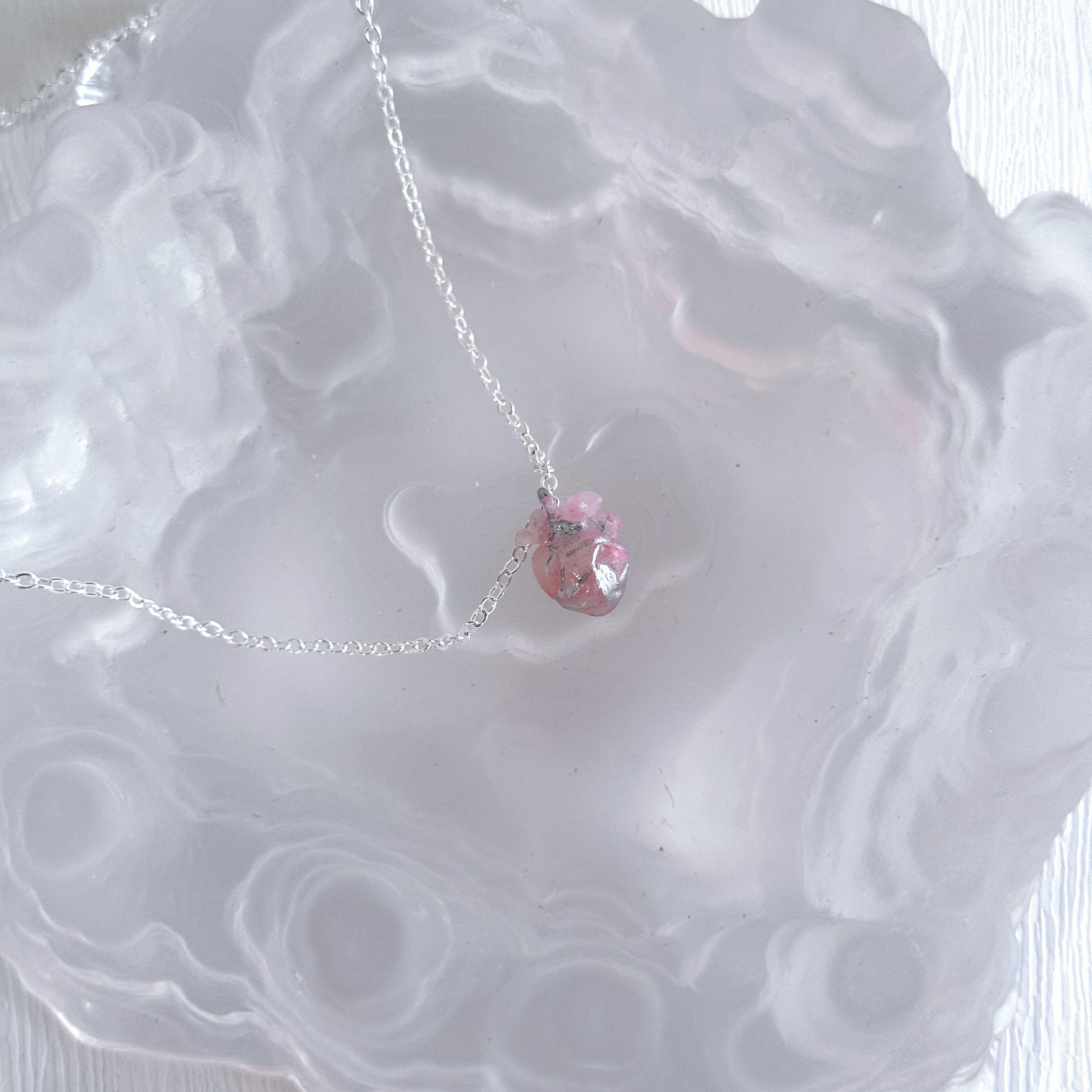 Necklace with a pink heart pendant on a textured white surface