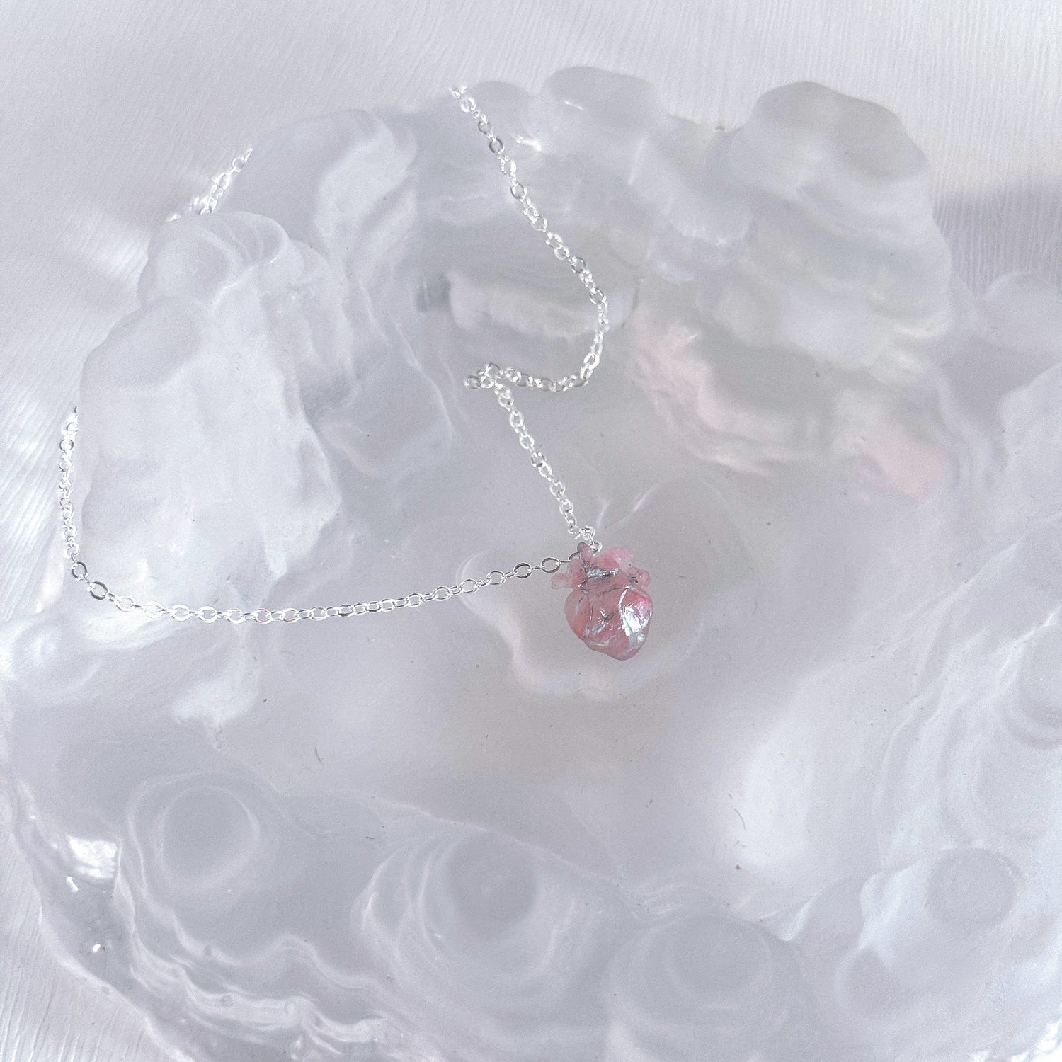 Necklace with a pink heart pendant on a white textured surface