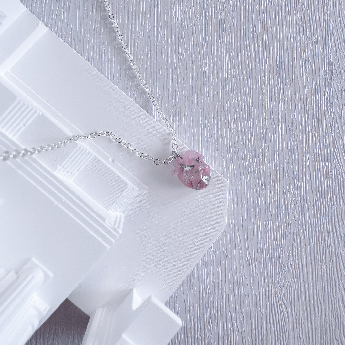 Necklace with a pink heart pendant on a white stand against a light gray background