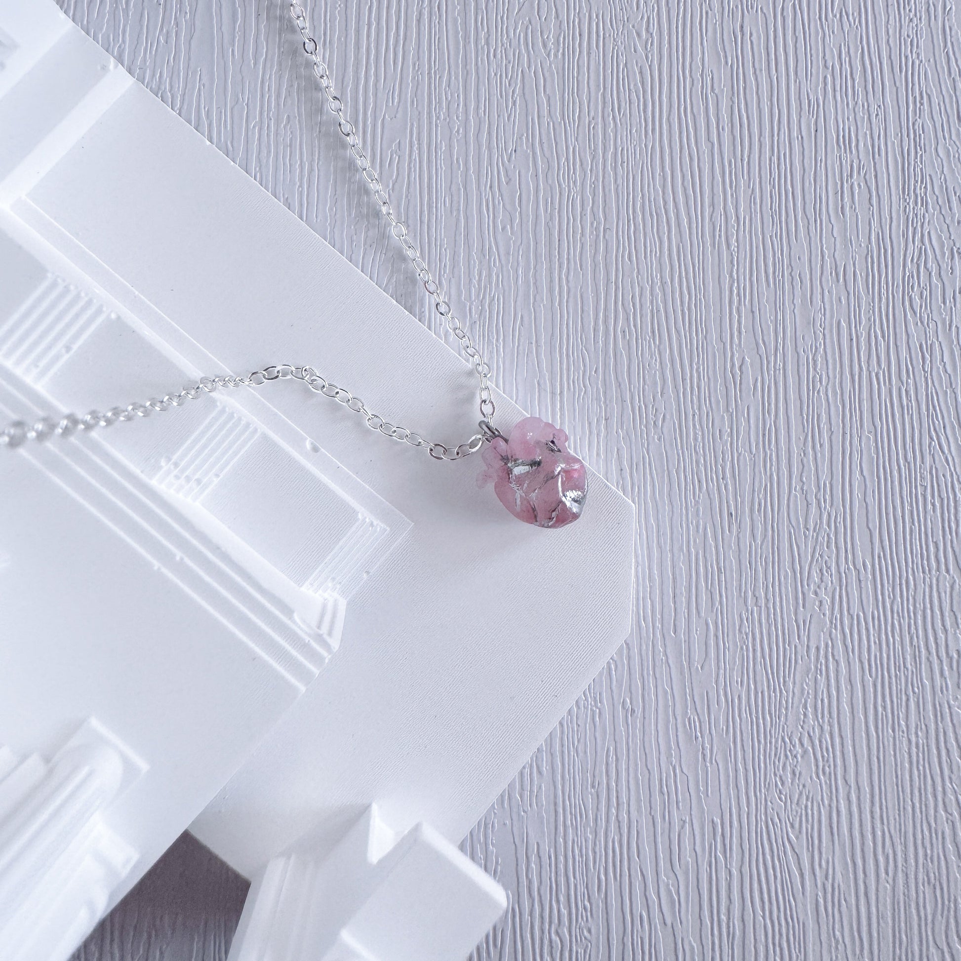 Necklace with a pink heart pendant on a white stand against a light gray background